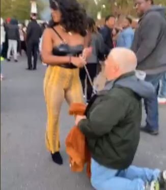 A man on a leash by a woman in the public to show she's a domme